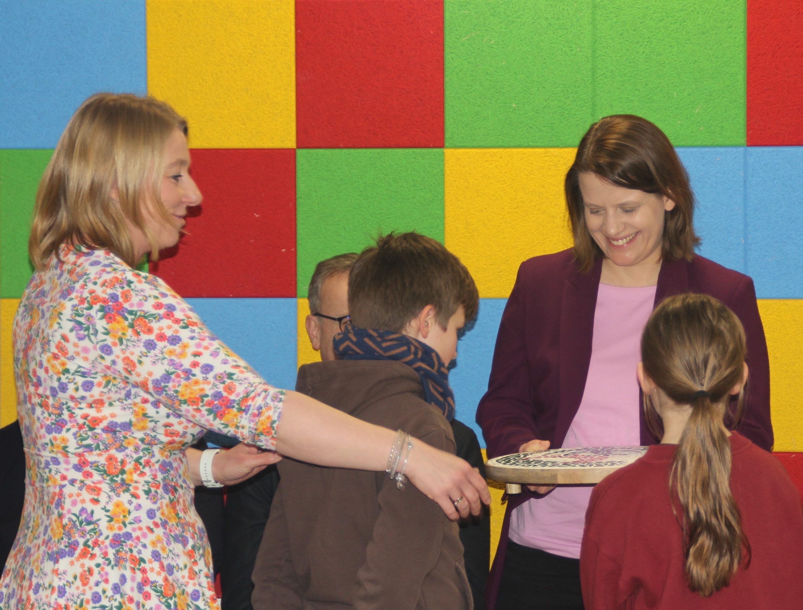 Kinder der Drei-Religionen-Schule überreichen zusammen mit der stellvertretenden Schulleiterin Sandra Wilhelm (links) ein Mosaik mit dem Schullogo an Kultusministerin Julia Willie Hamburg (rechts)